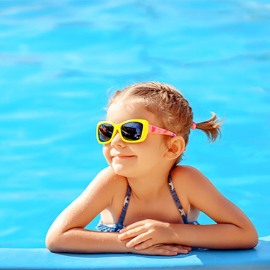 Malé dieťa sa smeje na okraji bazéna. Tvrdosť vody v bazénoch môže viesť k poškodeniu povrchov bazéna a ku korózii potrubí.